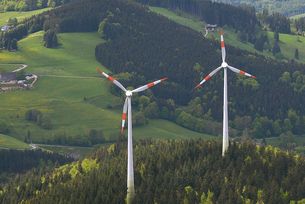 Windräder auf einem bewaldeten Hügel.
